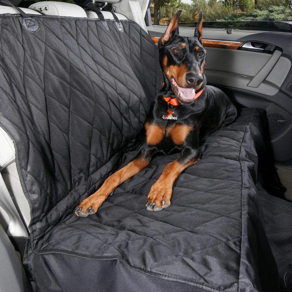 Doberman lying on a black quilted seat cover in hammock mode in a car's back seat