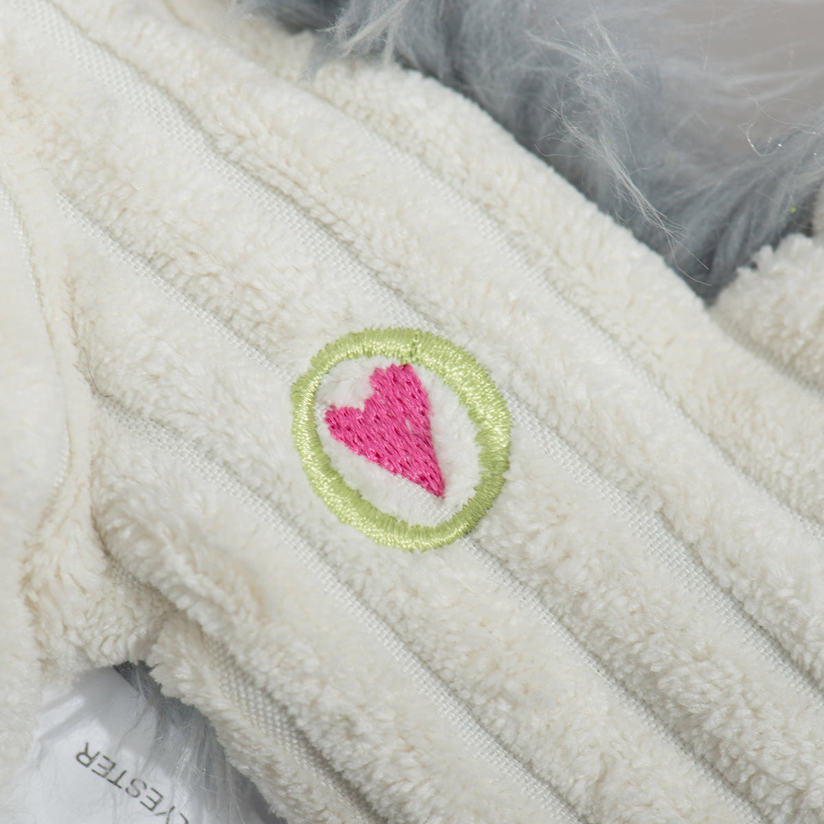 Close-up of the embroidered heart patch on the bunny toy's cream corduroy belly