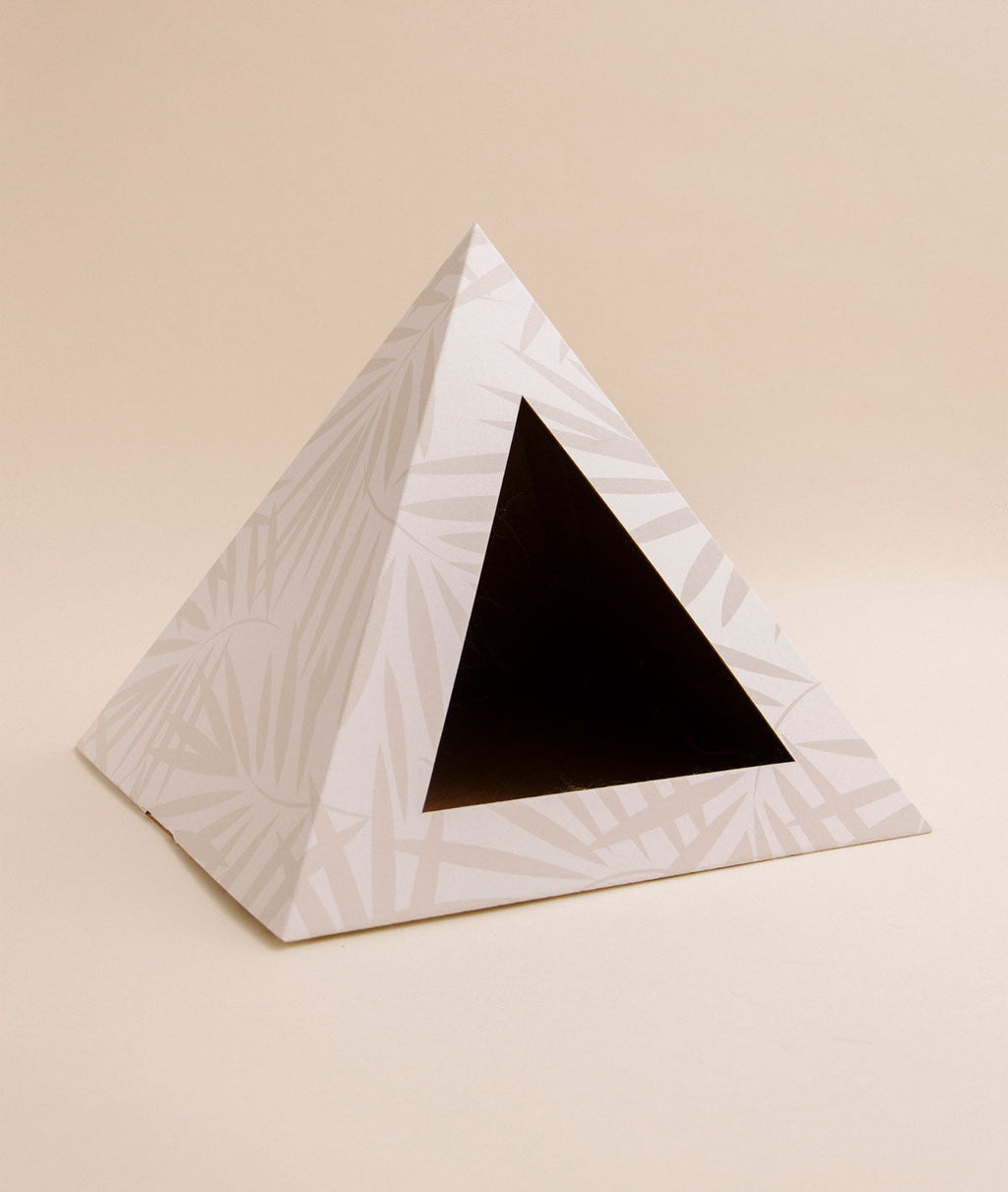 Empty cream cardboard cat pyramid with a pale palm-leaf print