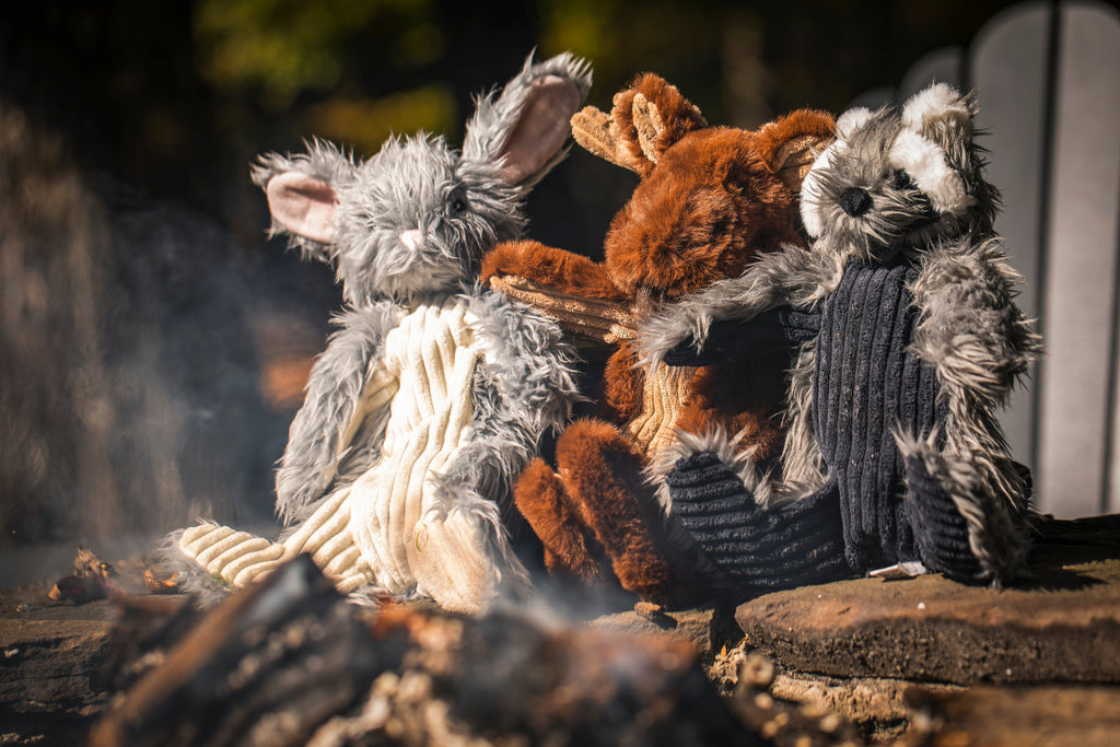 Bunny, fox and raccoon plush toys sitting together by a campfire