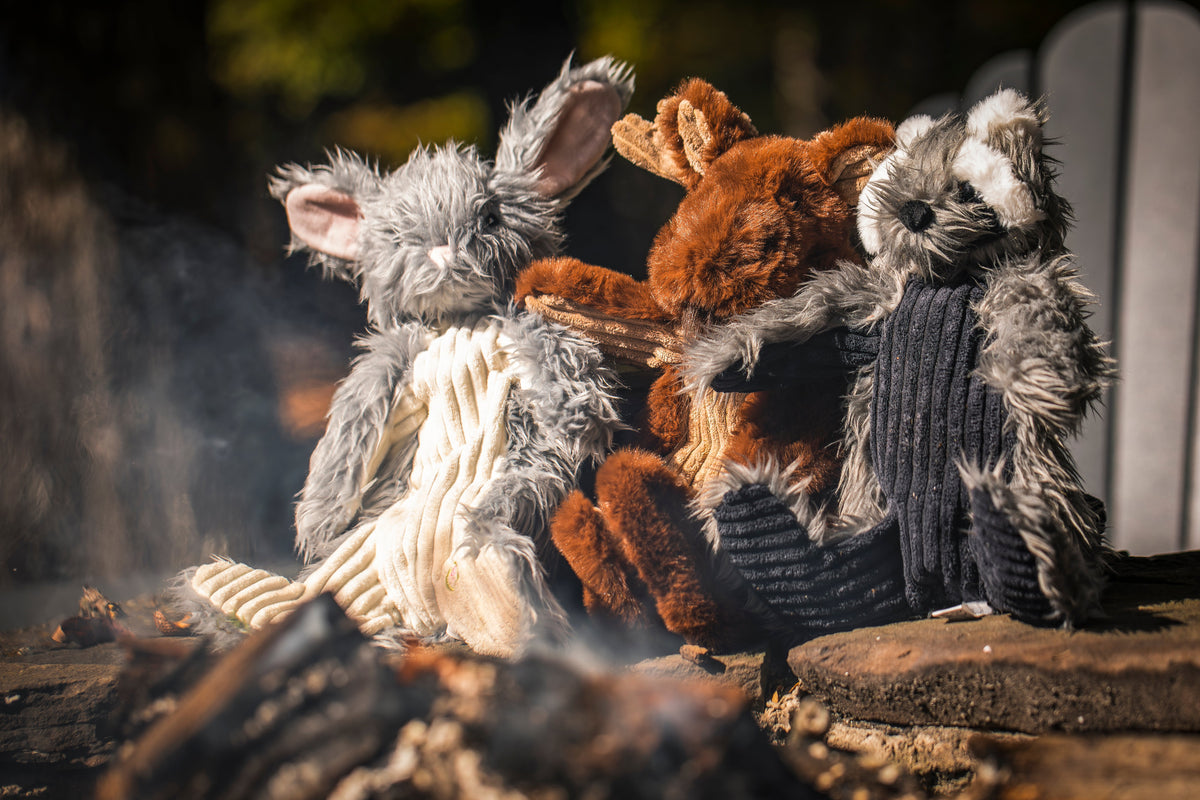 Bunny, fox and raccoon plush toys sitting together by a campfire