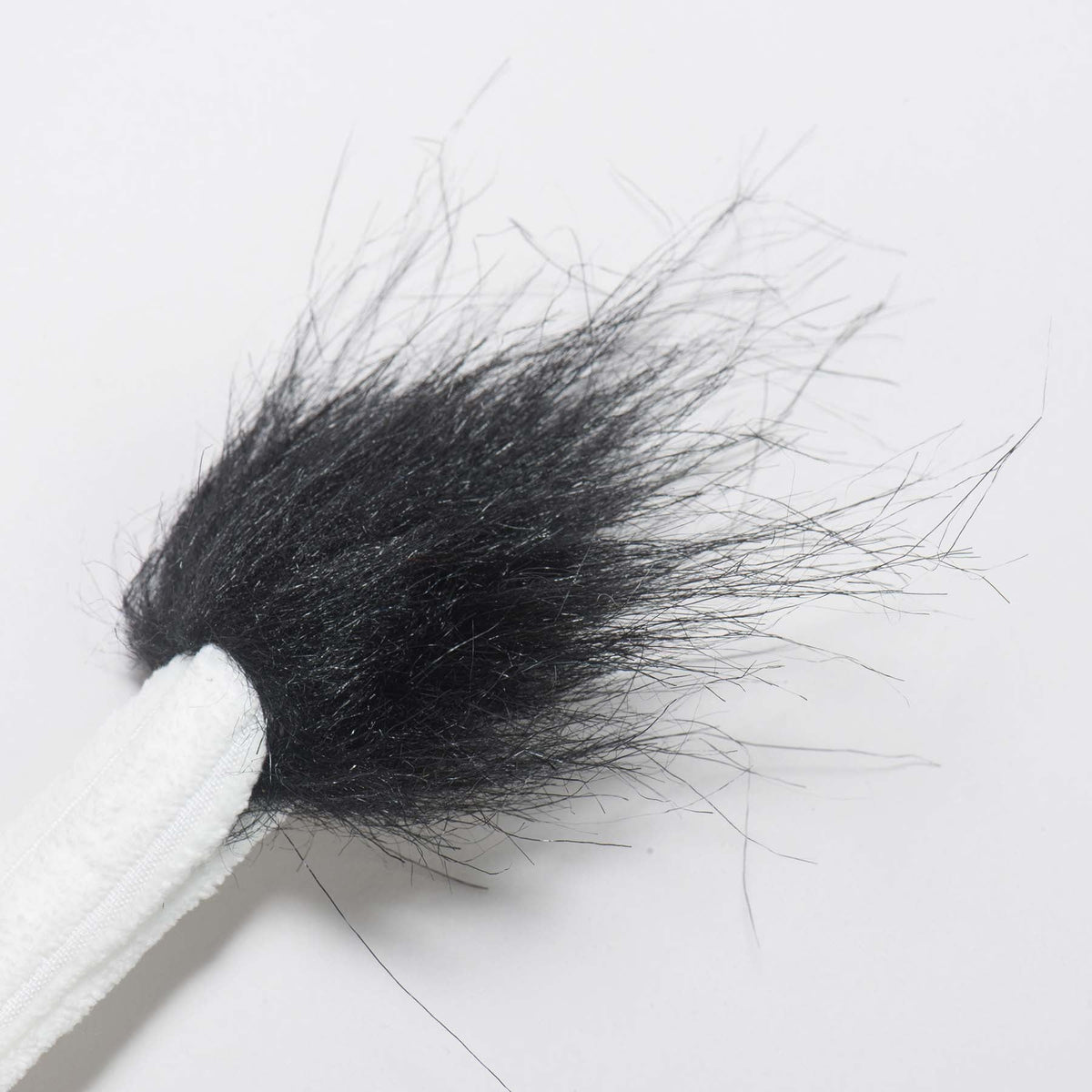 Close-up of the cow toy's white corduroy tail ending in a black furry tuft