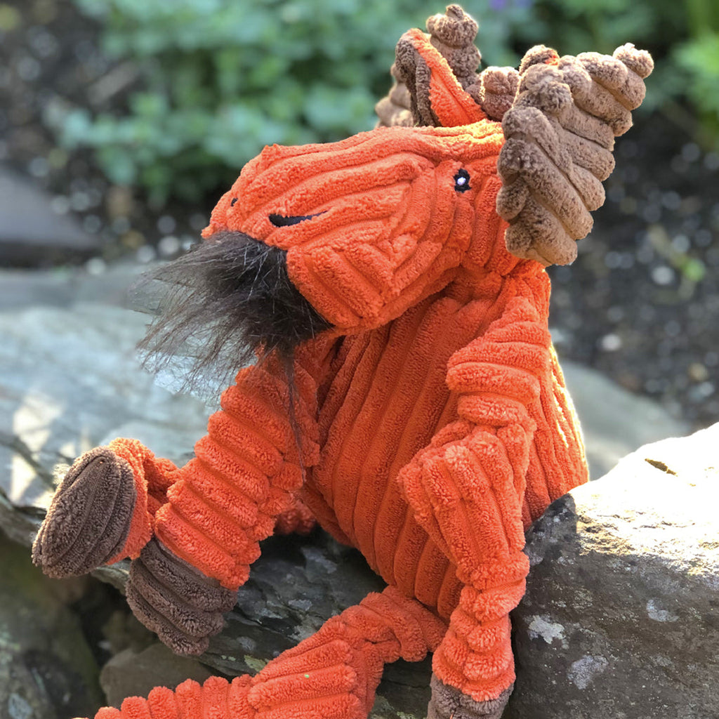 Orange moose plush dog toy sitting on a rock in a garden