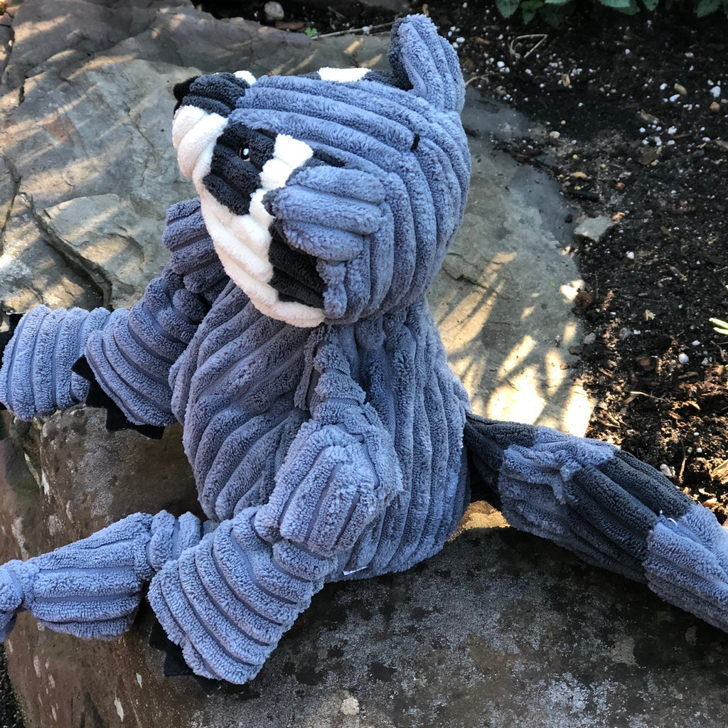 Raccoon plush dog toy sitting on a rock outdoors