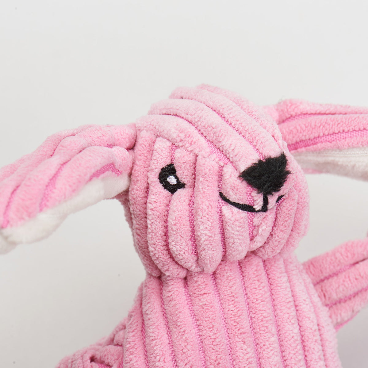 Close-up of the pink bunny toy's embroidered face and corduroy texture