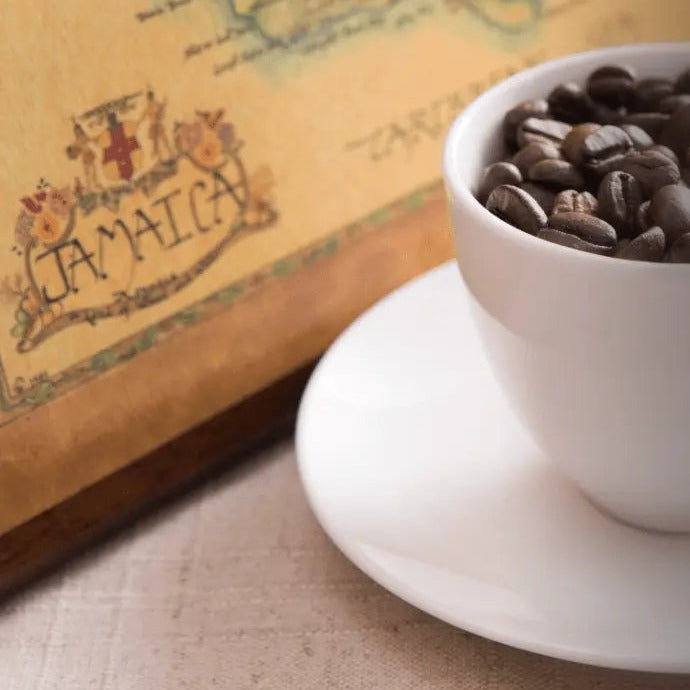 Cup of whole coffee beans on a saucer in front of a vintage map of Jamaica