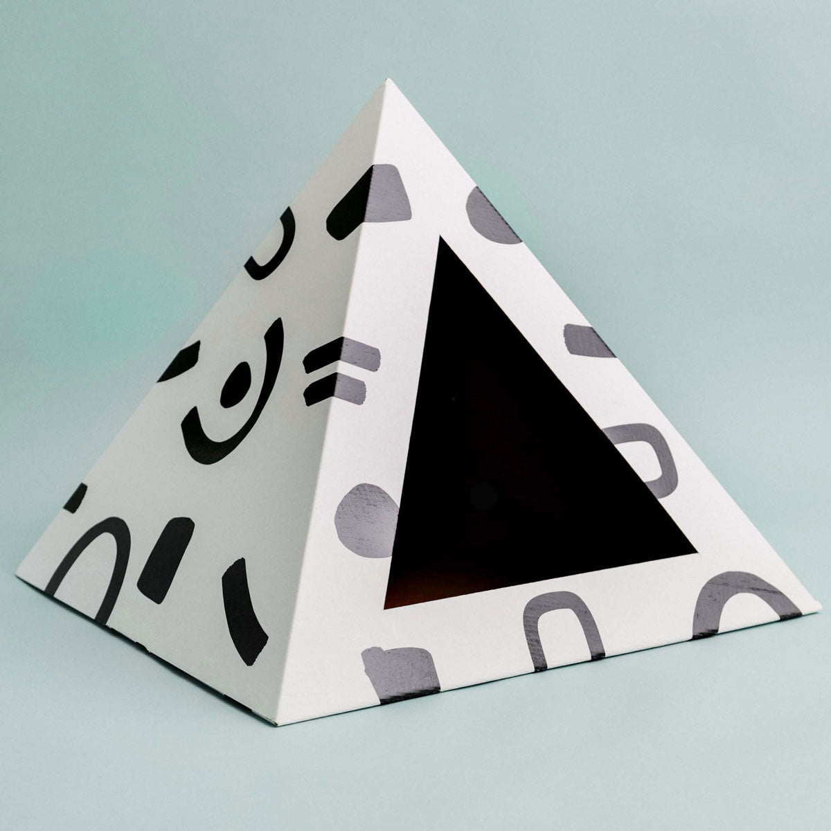 White cardboard cat pyramid with black doodle pattern and a triangle doorway