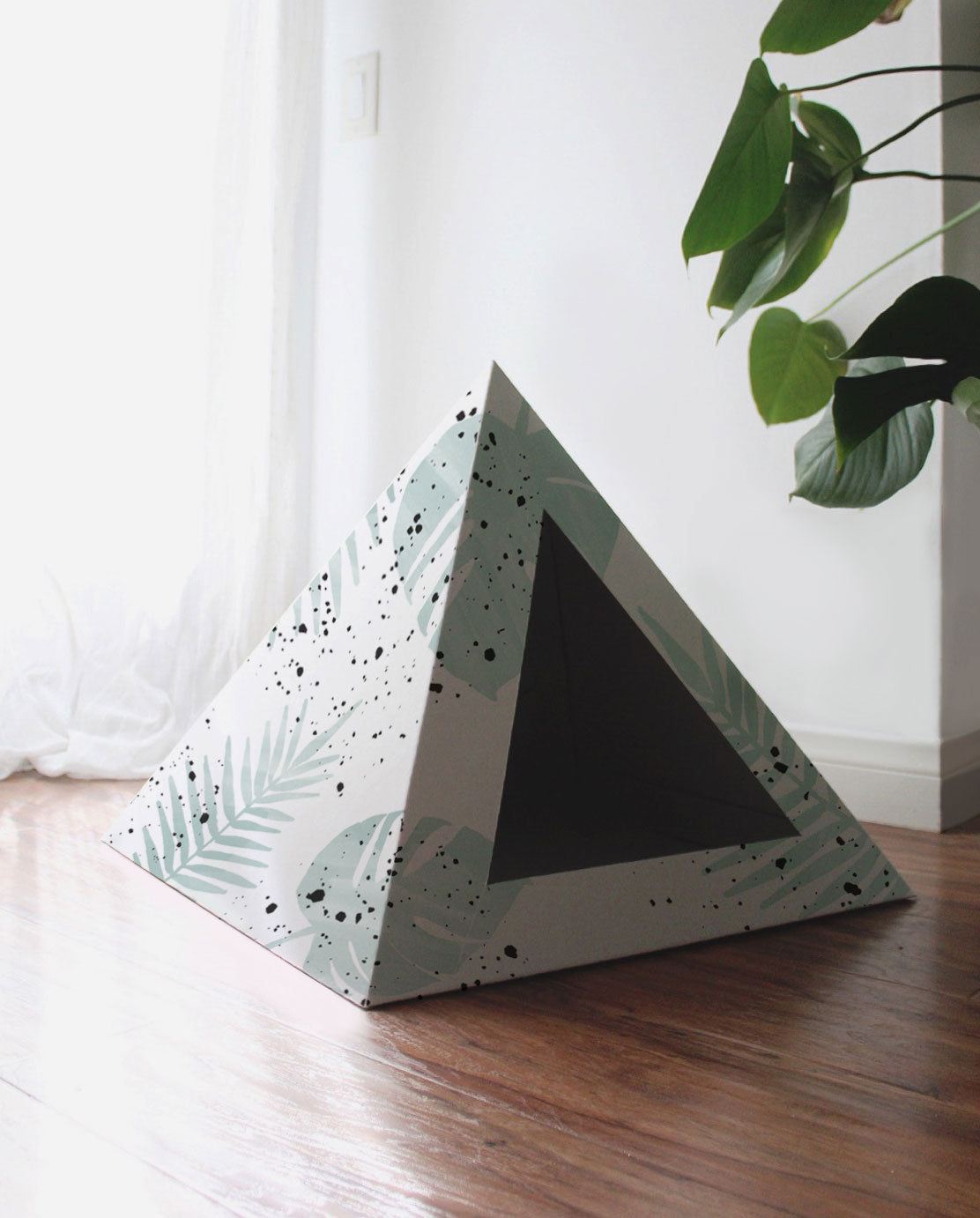 Empty leaf-print cardboard cat pyramid on a wood floor by a window