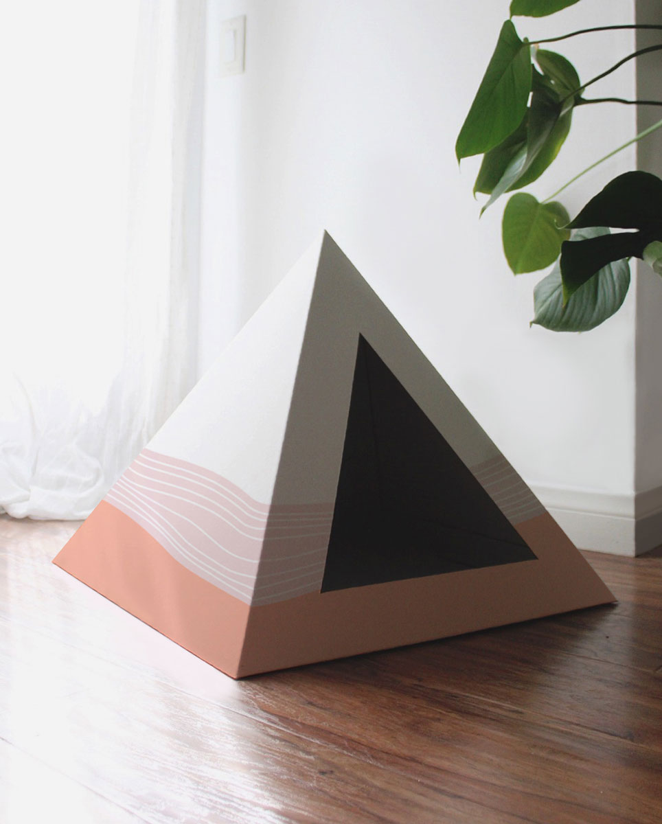 Empty Wavey cardboard cat pyramid with a white top fading to peach on a wooden floor