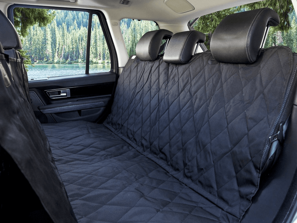 Black quilted dog seat cover fitted across an SUV's back seat, with a lake visible through the windows