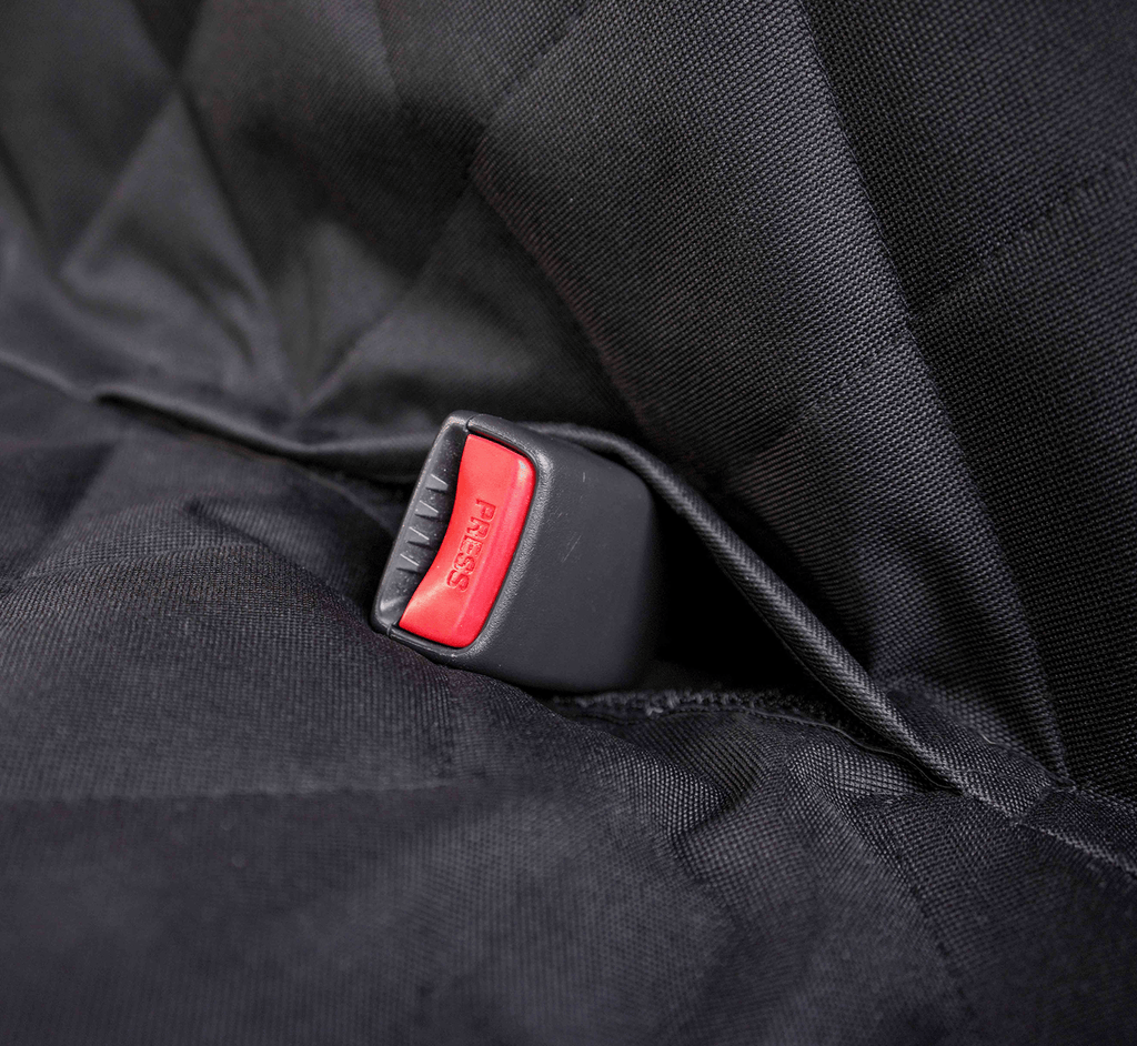 A red seat belt buckle coming through an opening in the black quilted seat cover