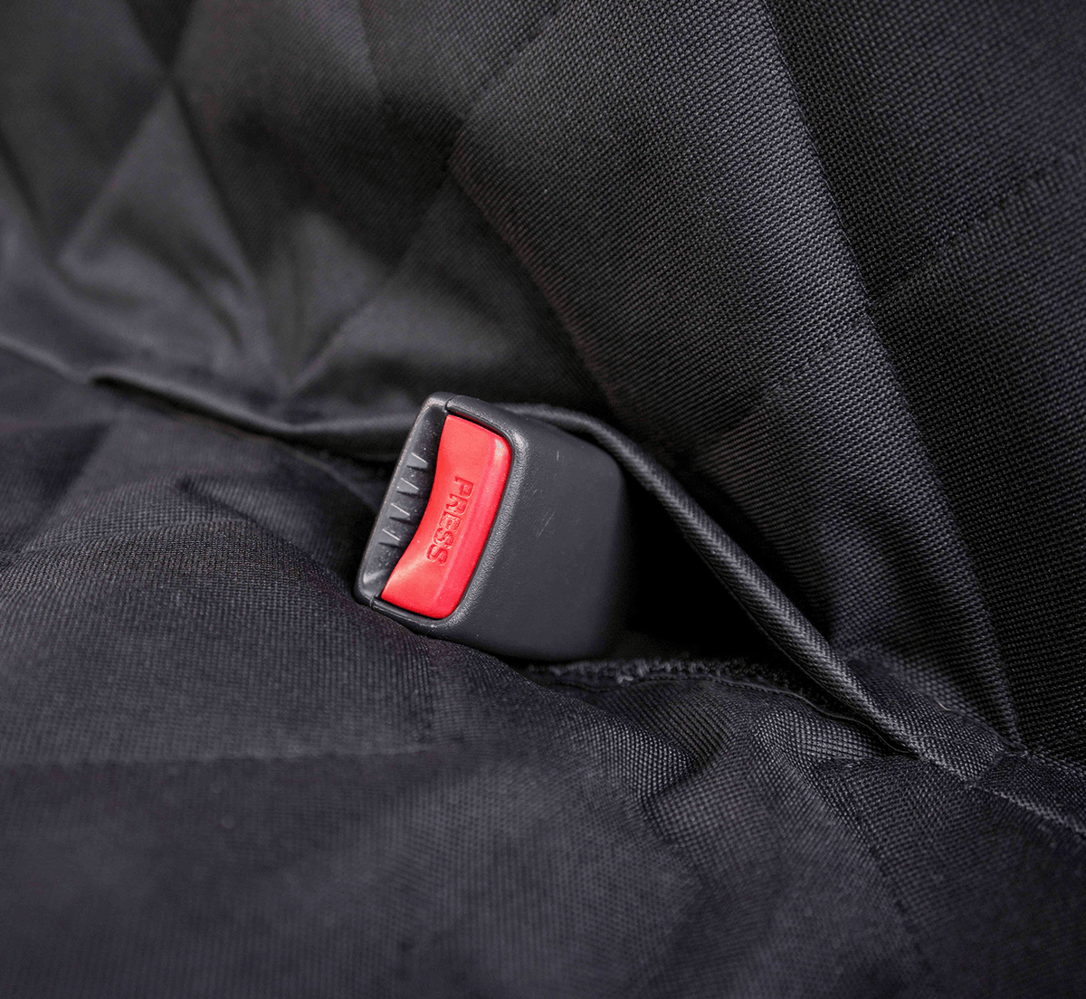 A red seat belt buckle coming through an opening in the black quilted seat cover