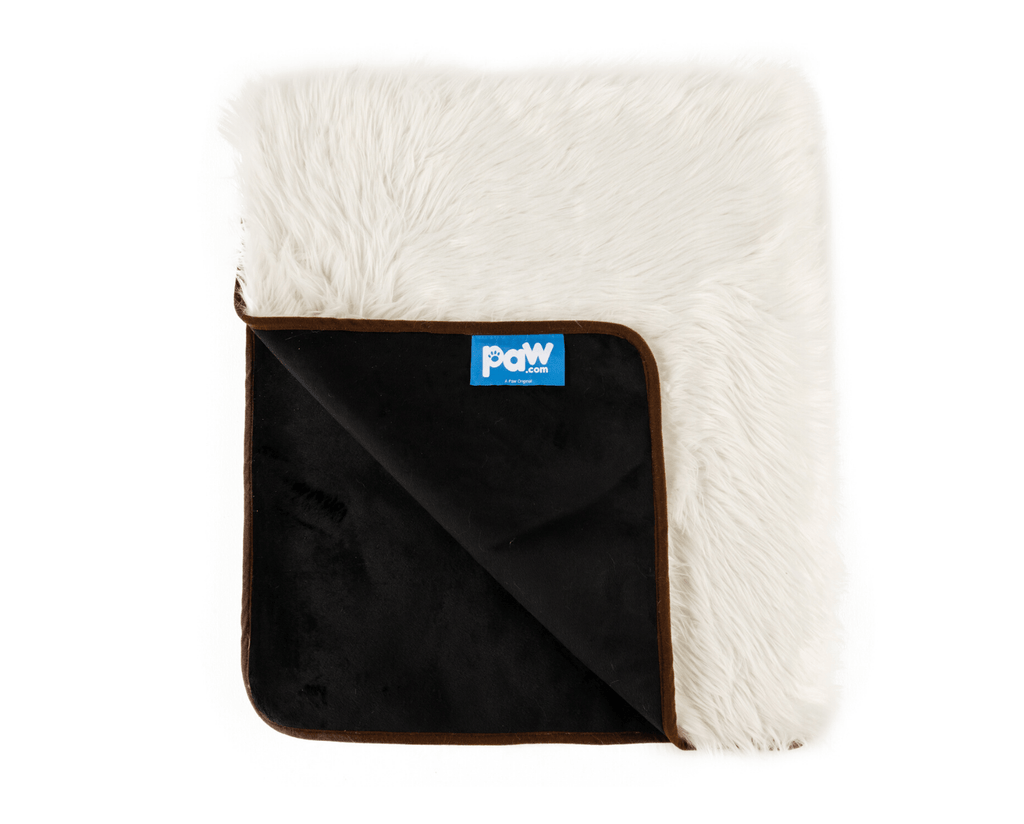 Folded corner of the polar white throw, showing white faux fur and the black microsuede back with brown trim