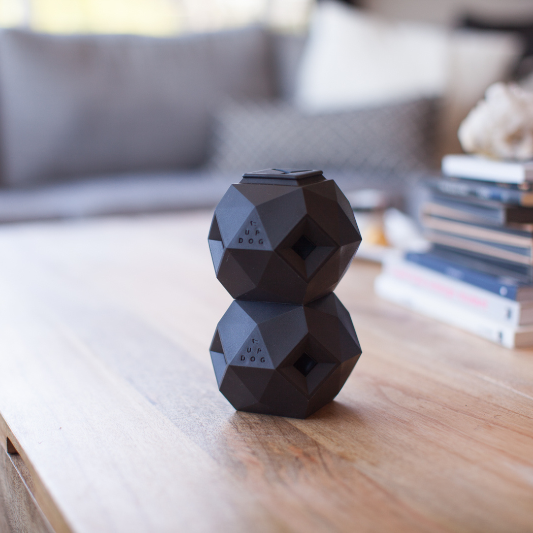 Two dark geometric treat toys stacked on a wooden table