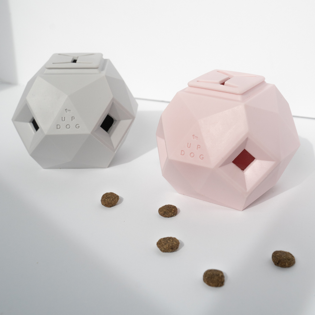Gray and pink geometric treat dispensing dog toys with kibble scattered around