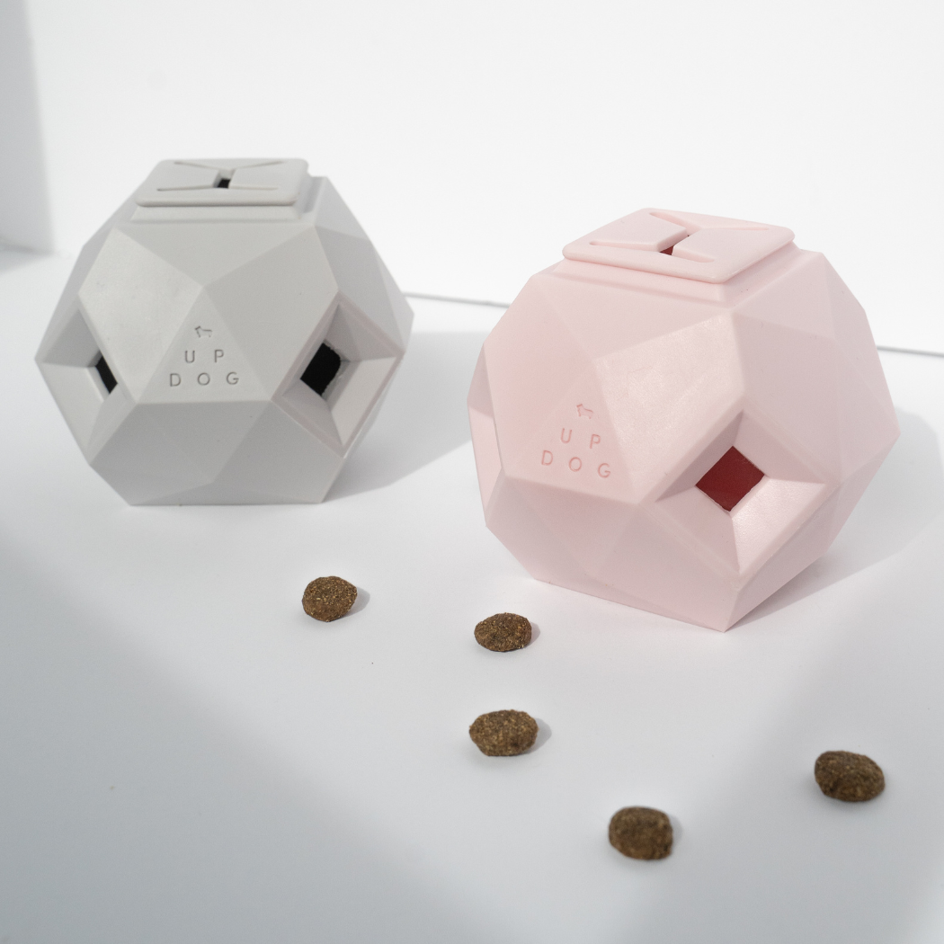 Gray and pink geometric treat dispensing dog toys with kibble scattered around