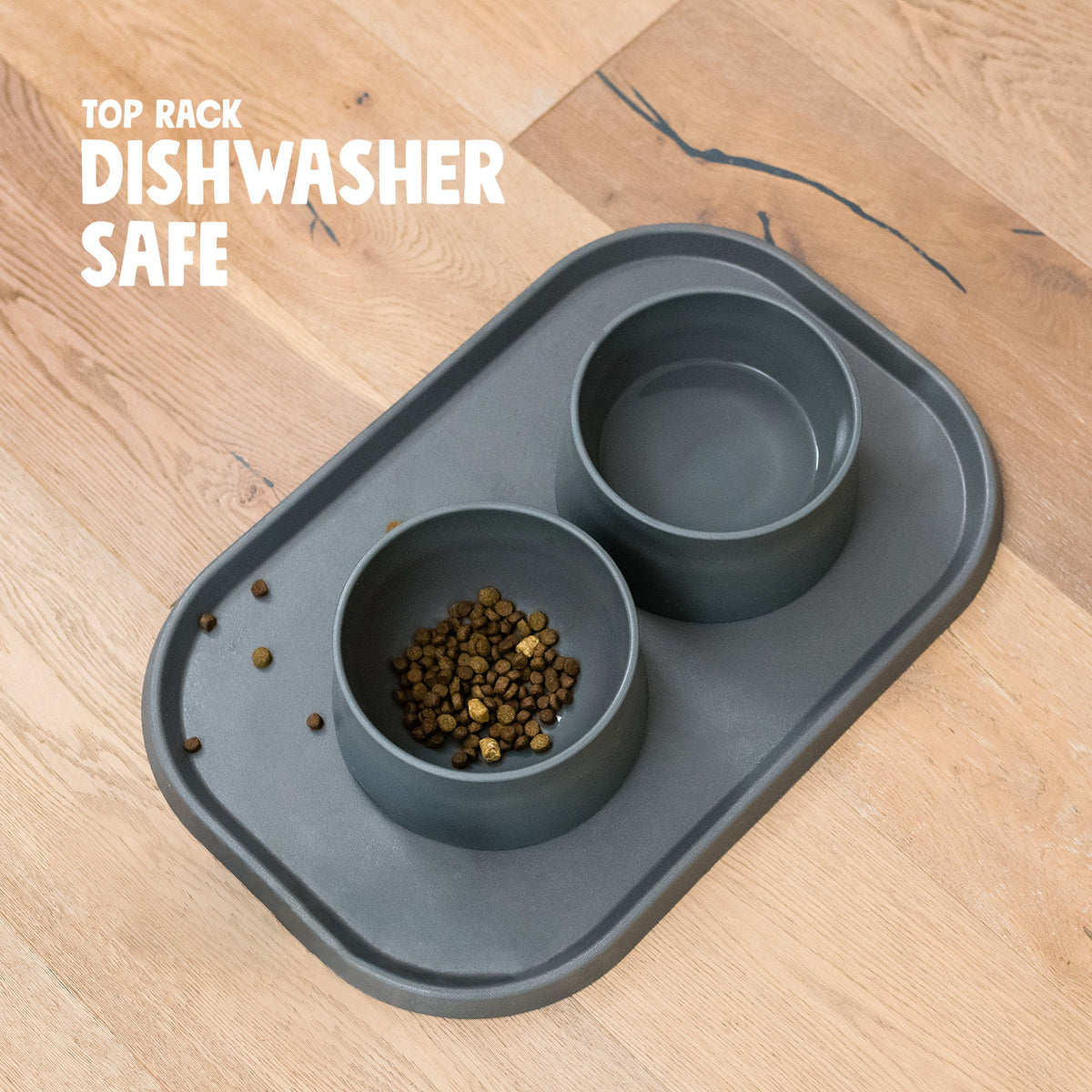 Charcoal placemat with two bowls, one holding kibble, on a wood floor
