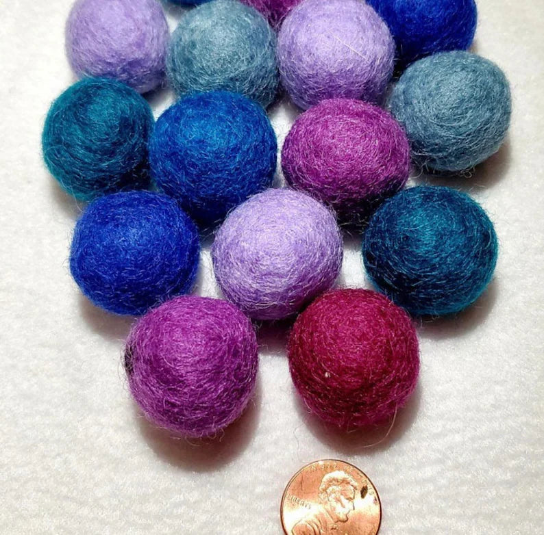 Felted wool cat balls in purple and blue next to a penny for size